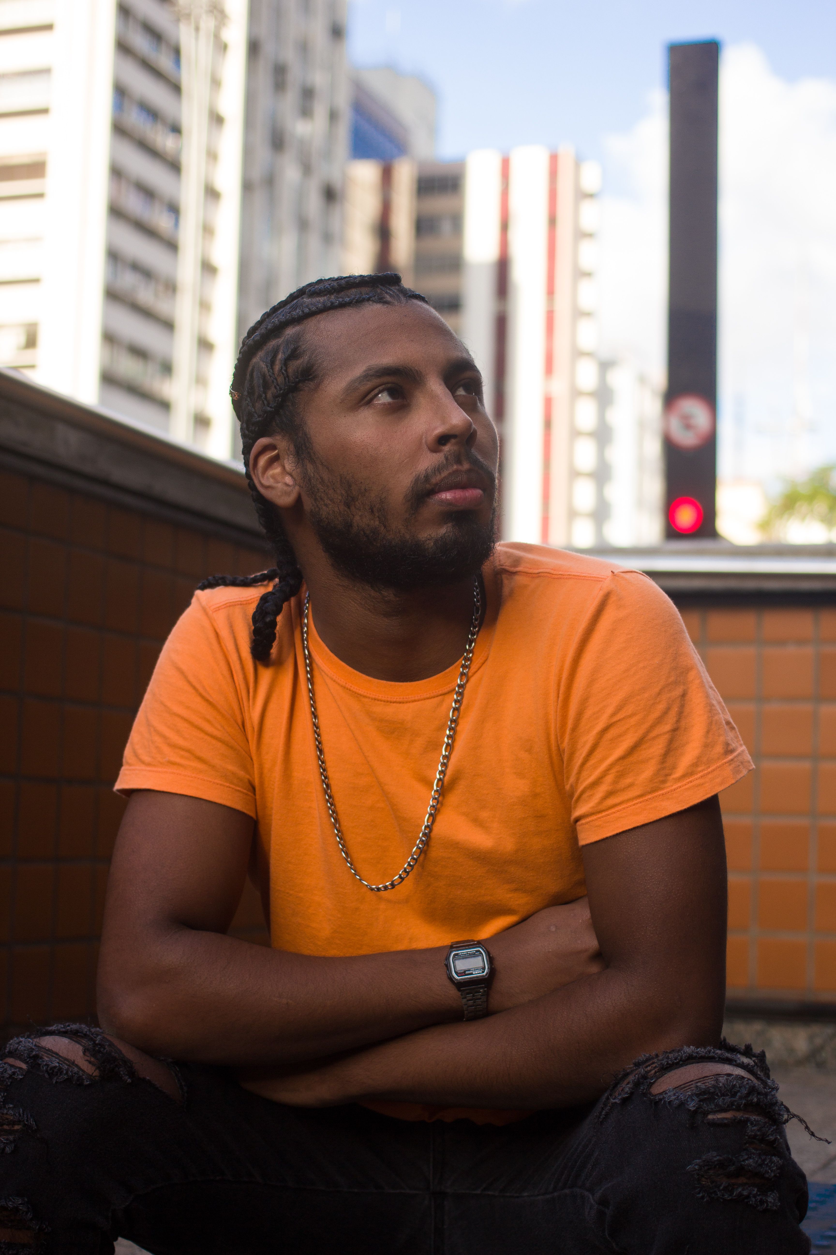 A thoughtful man in a yellow shirt sits with arms crossed in São Paulo's urban landscape.