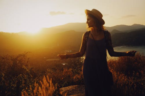 Woman Wearing a Summer Hat Standing in a Field in Sunset
