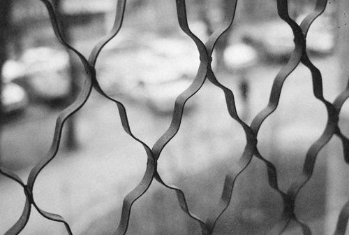 Free Blurred urban background through a patterned metal fence in black and white, creating an abstract look. Stock Photo