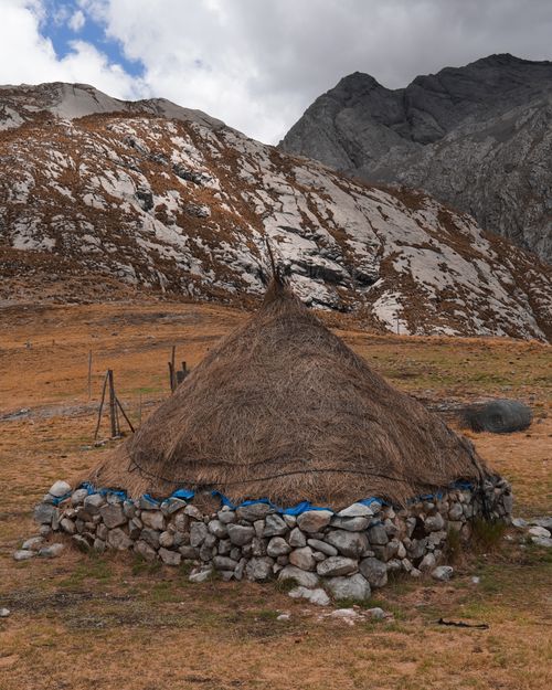 Free Scenic view of a rustic stone and hay hut surrounded by mountains and rocky landscape. Stock Photo