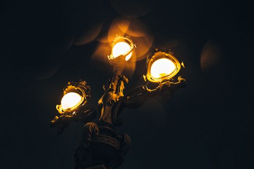 Free A close-up of a vintage street lamp illuminating the night sky with warm glowing lights. Stock Photo