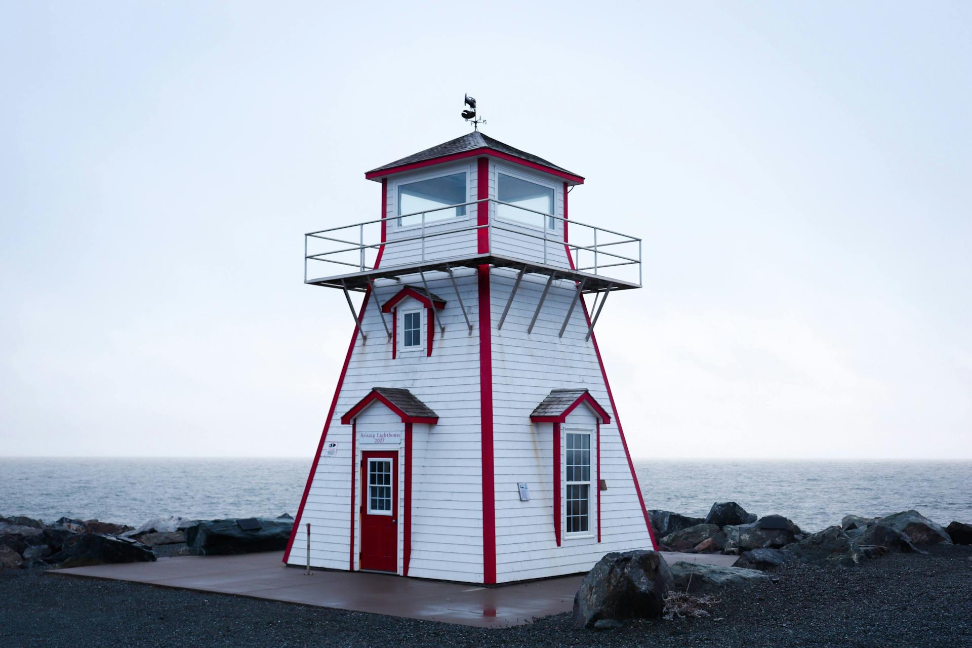 White and red lighthouse stands by the rocky ocean shore.
