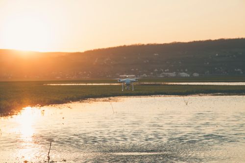 Free A serene landscape with a drone hovering over a lake during sunset, creating a peaceful atmosphere. Stock Photo