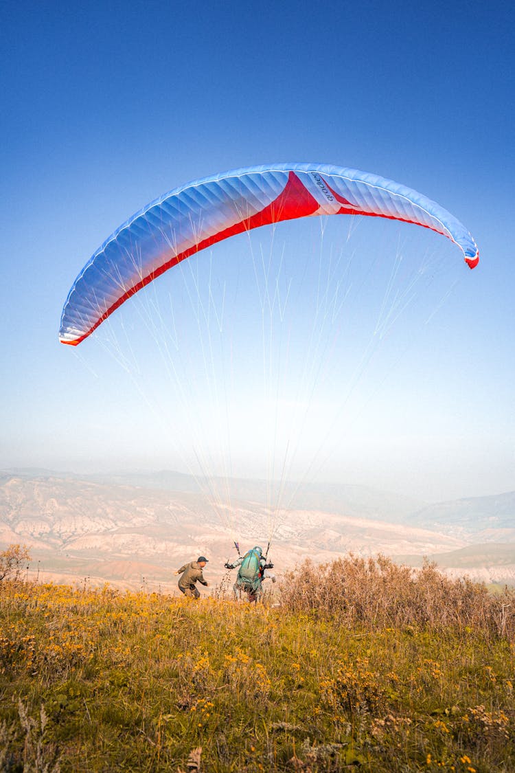 Man With A Parachute Jumping On Mountain Cliff