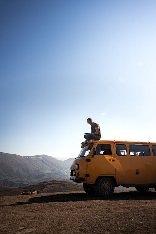 Free Photo of a Man Sitting on Top of a Yellow Van Stock Photo