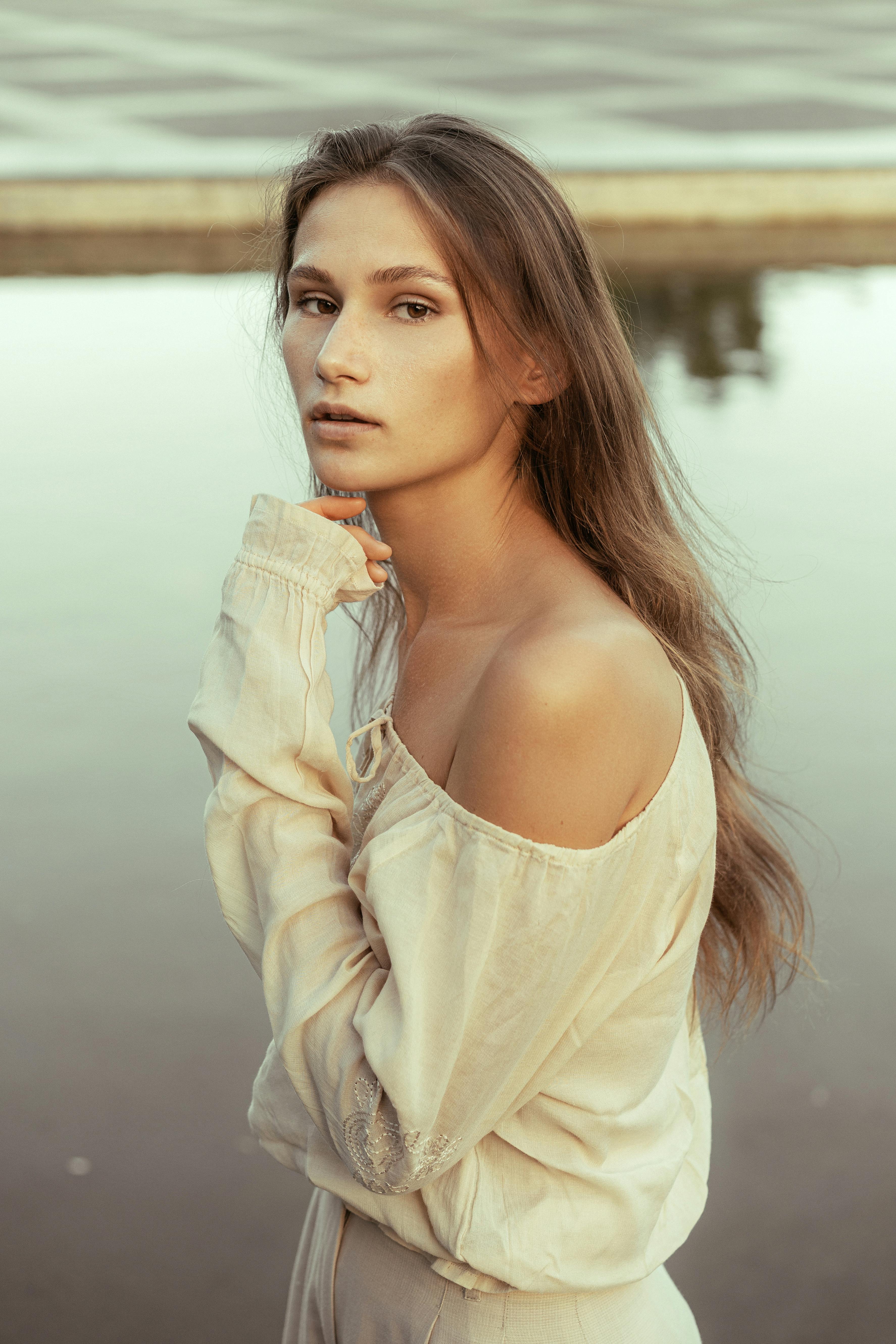 woman with long hair standing by water looking at camera