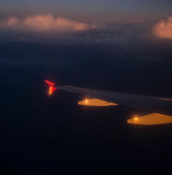 View of an airplane wing illuminated at night with clouds visible in the sky.