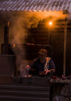 A street vendor grilling food at night under warm light in an outdoor stall.