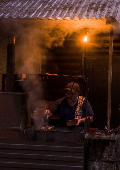 Free A street vendor grilling food at night under warm light in an outdoor stall. Stock Photo