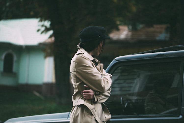 Person In Trench Coat Staring At Their Reflection In Car Window