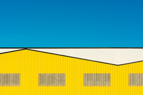Free Minimalist yellow warehouse facade against bright blue sky Stock Photo