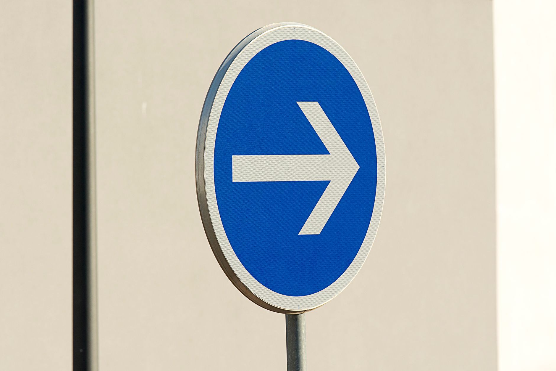 Close-up of a blue directional arrow traffic sign against a neutral background.