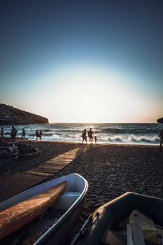 A beautiful evening beach scene with tourists enjoying the sunset near boats by the sea.