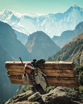 A Sherpa man carries wooden planks in the Himalayas with stunning mountain scenery.