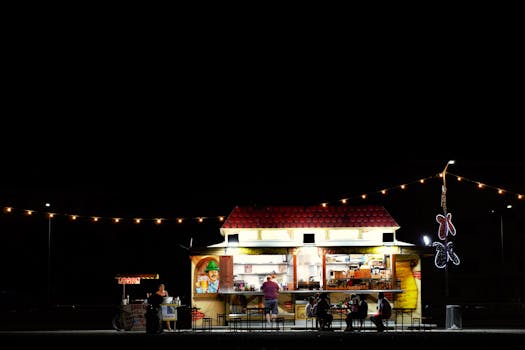 Outdoor dining at a vibrant food cart illuminated by string lights under a dark sky.