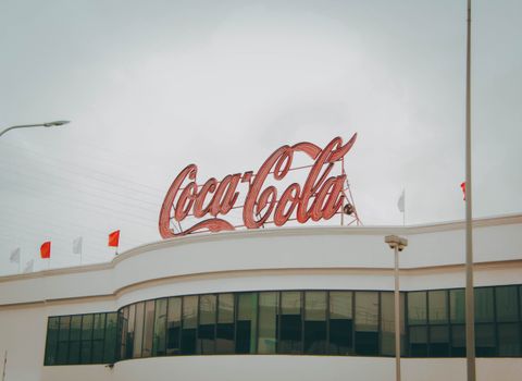 Exterior view of Coca-Cola factory with iconic red sign atop the modern building. 9973155