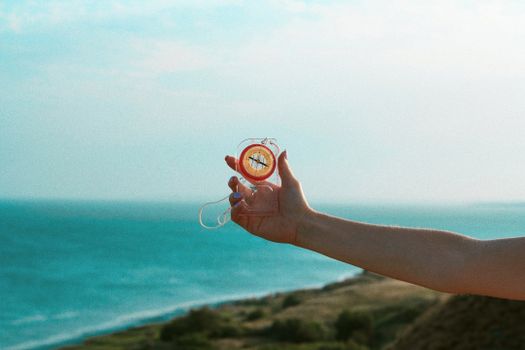 An outstretched arm holding a compass against a backdrop of the blue ocean and horizon.