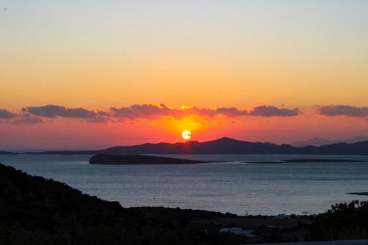 Serene sunset casting vibrant hues over calm sea and distant islands.