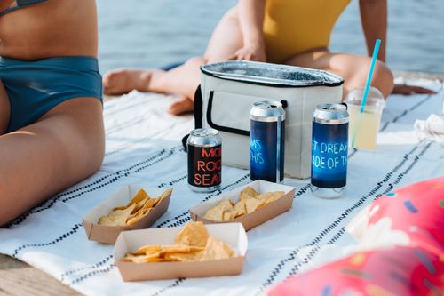 Free Relaxing summer picnic by the water with snacks, drinks, and swimwear. Stock Photo
