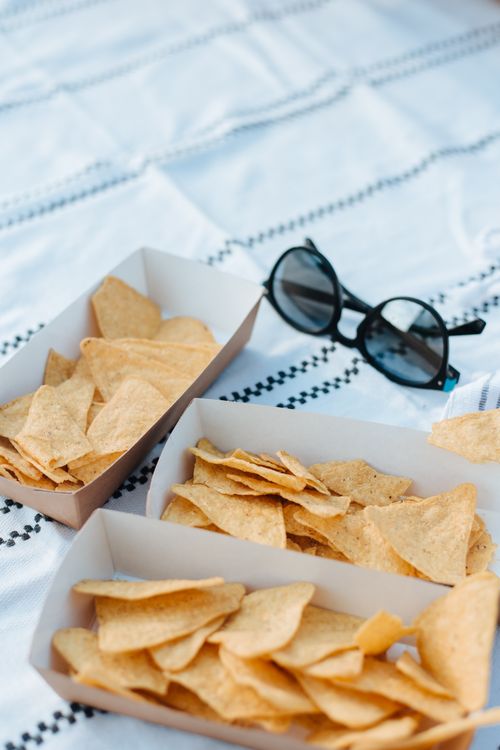 Free Tortilla chips in paper containers on a picnic blanket with sunglasses, perfect for outdoor gatherings. Stock Photo