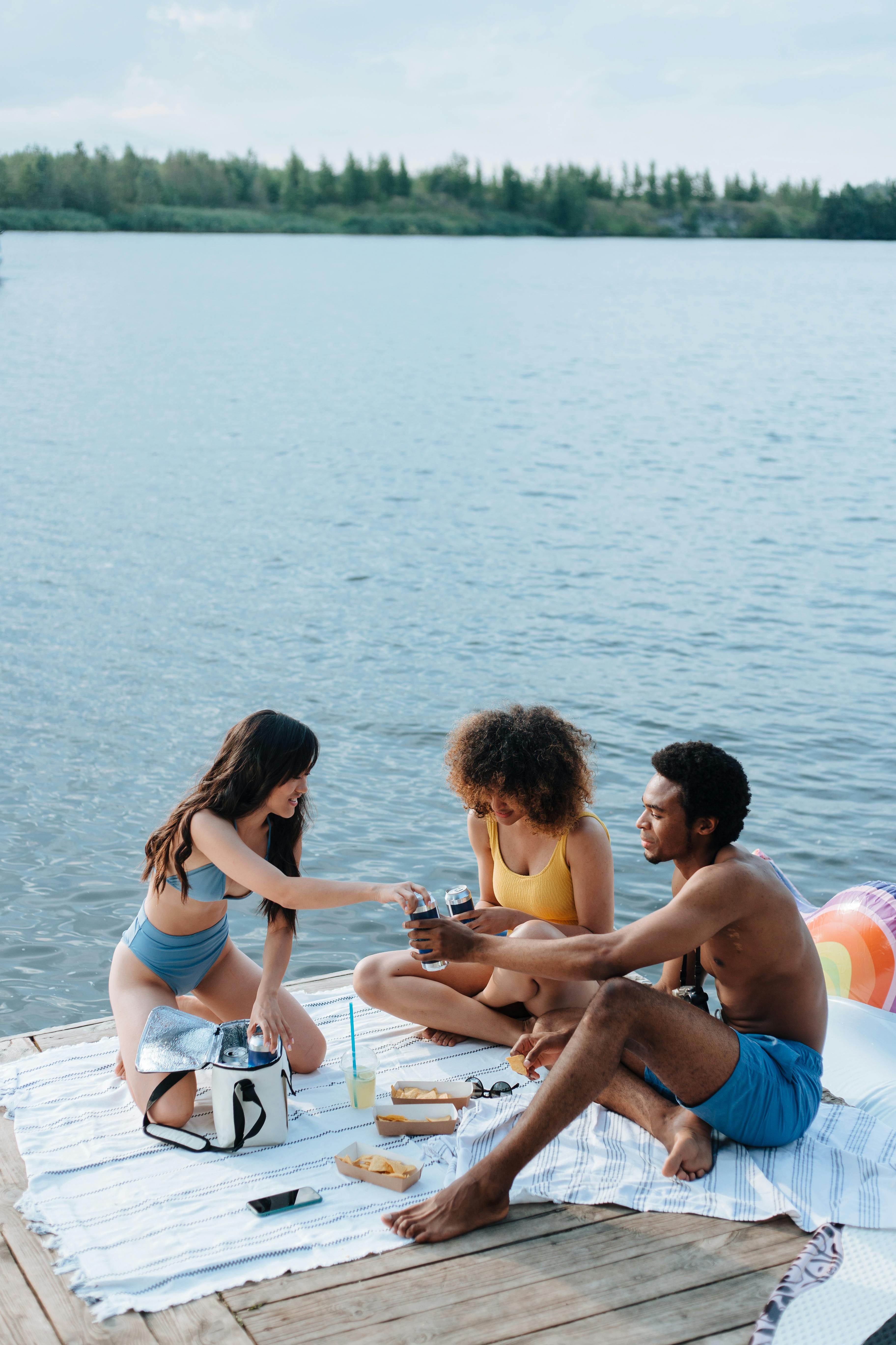 Three friends having a fun picnic on a lakeside dock during summer.
