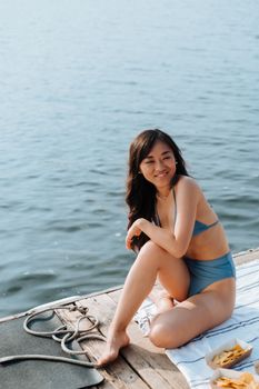 A cheerful woman in a swimsuit sits on a pier by a serene lake. Ideal for summer lifestyle themes.