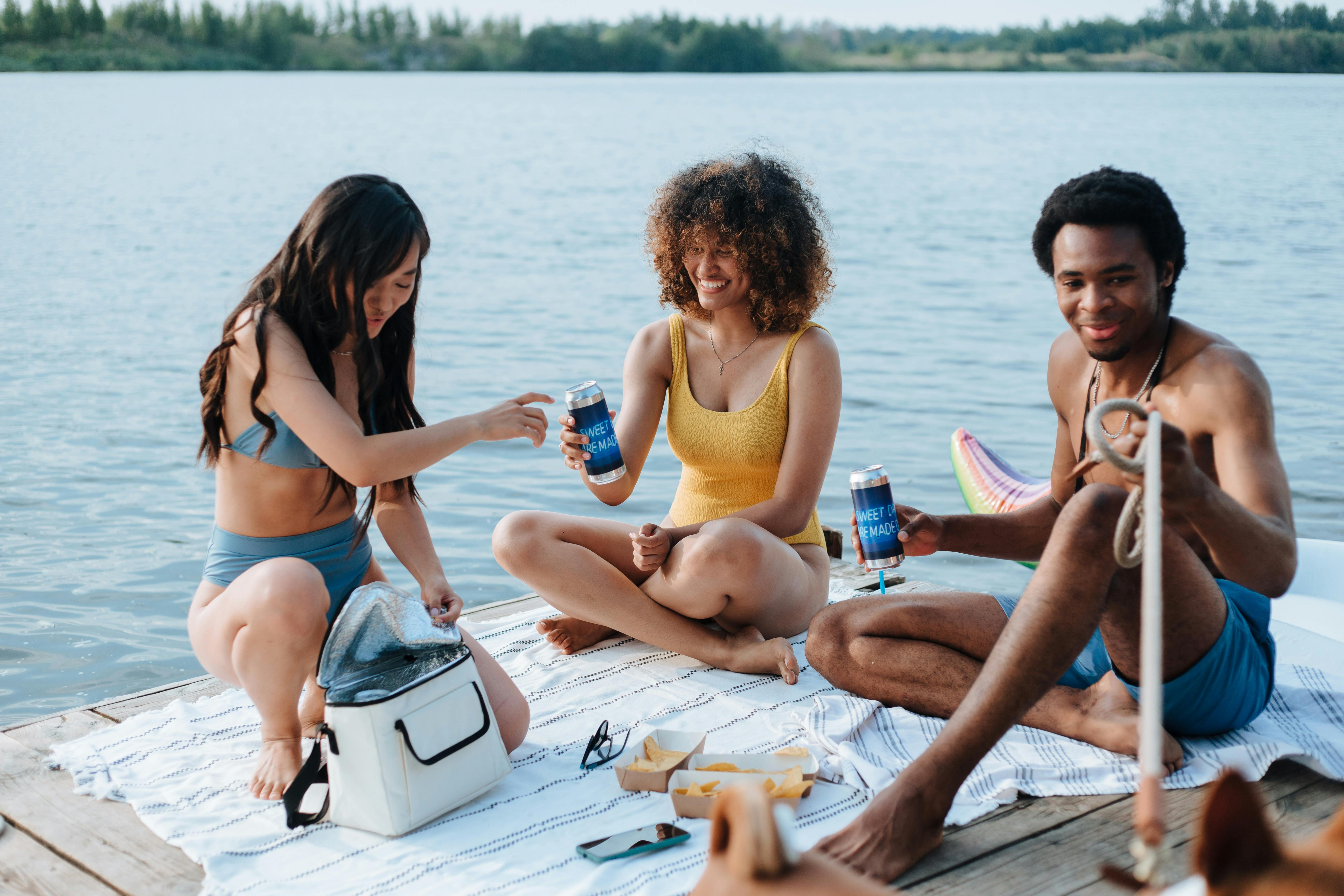 Diverse group of friends relaxing with drinks on a lakeside dock, enjoying a summer day.