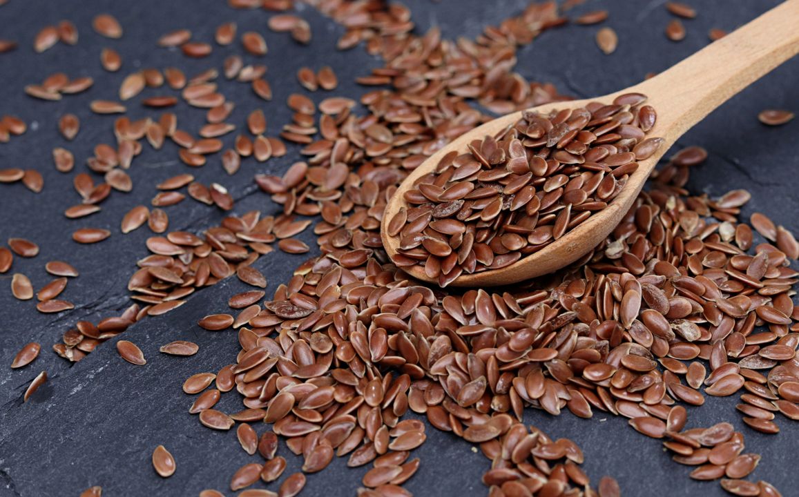 Eggless Baking: The Complete Substitute Guide for Every Recipe 3 Brown flax seeds scattered on a slate surface next to a wooden spoon — one of the most reliable eggless binding agents available in Indian kitchens.