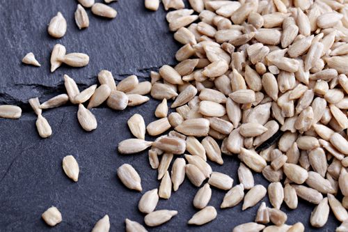 Free A detailed close-up image of organic sunflower seeds scattered on a slate surface, highlighting texture and freshness. Stock Photo