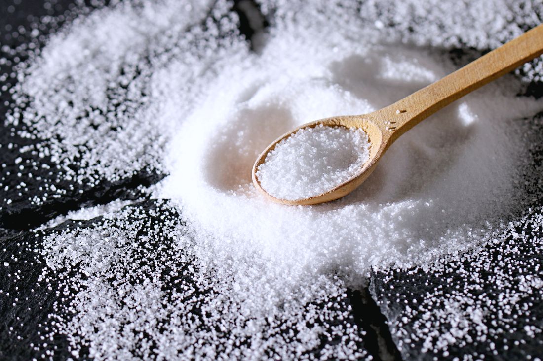 Fine white sea salt spilled on dark slate with wooden spoon