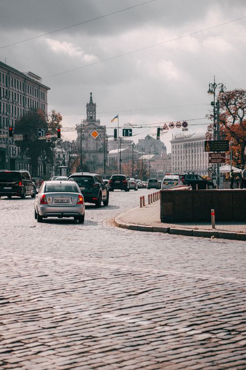 Free City traffic on a cobblestone street under a cloudy sky, showcasing urban architecture. Stock Photo