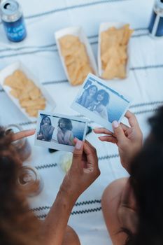 Two women enjoy reminiscing with photos and snacks in a sunny outdoor setting.
