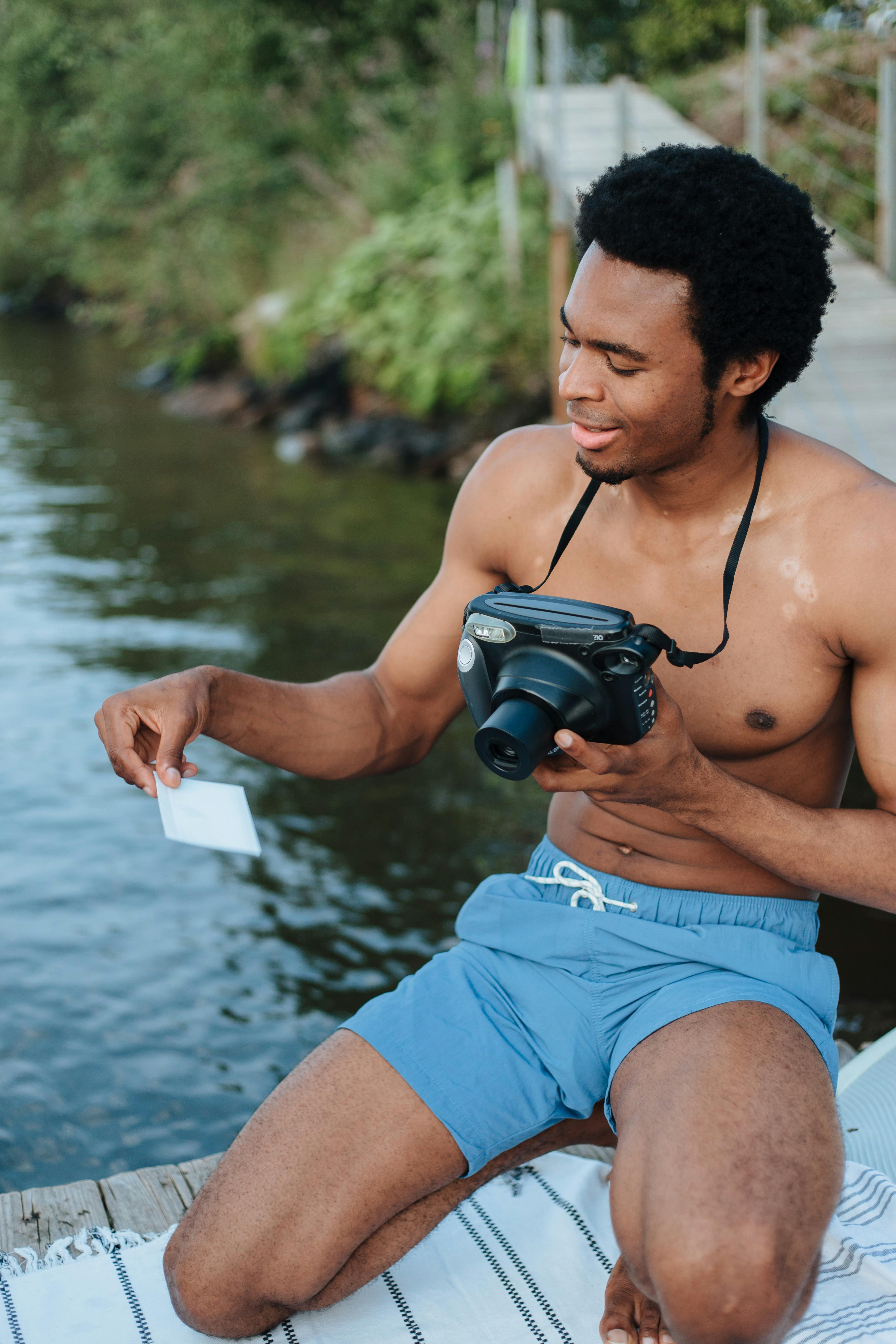 Man sitting by the lakeside with an instant camera, capturing summer memories.