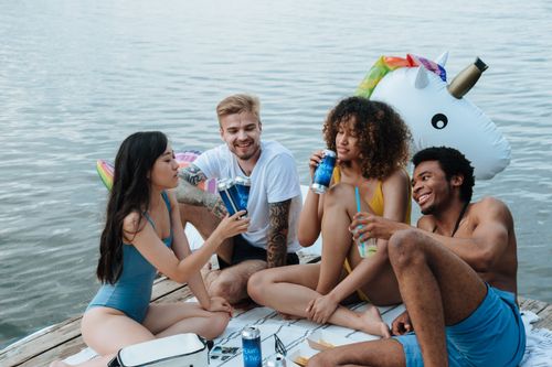 Free Group of friends relaxing on a dock with drinks during summer near a lake. Stock Photo