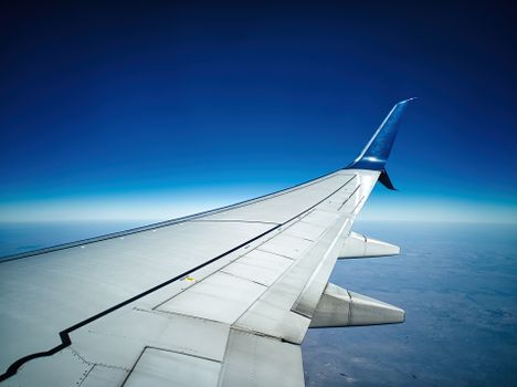 View of airplane wing from window seat, showcasing clear sky and horizon.