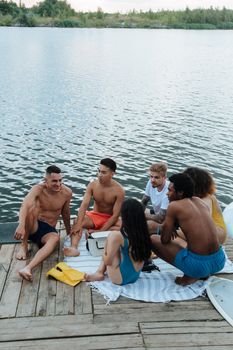 Diverse group of friends enjoying leisure time by the lakeside, seated on a dock outdoors.