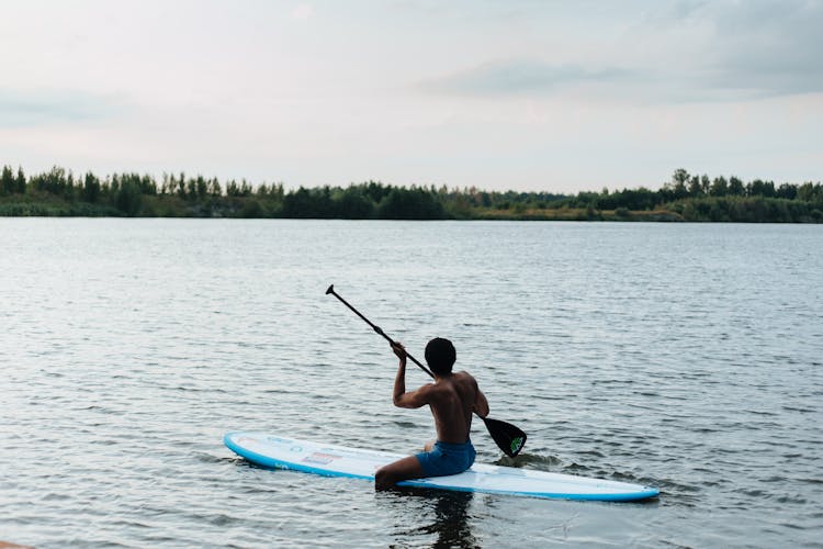 Man Sitting On Paddleboard And Rowing