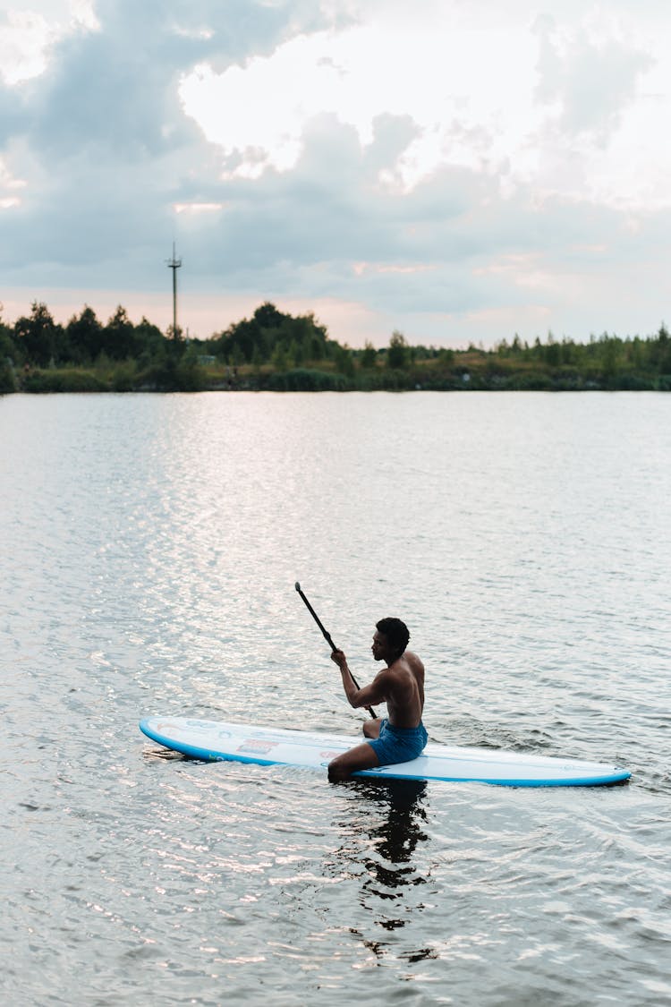 Man Sitting On Paddleboard And Rowing