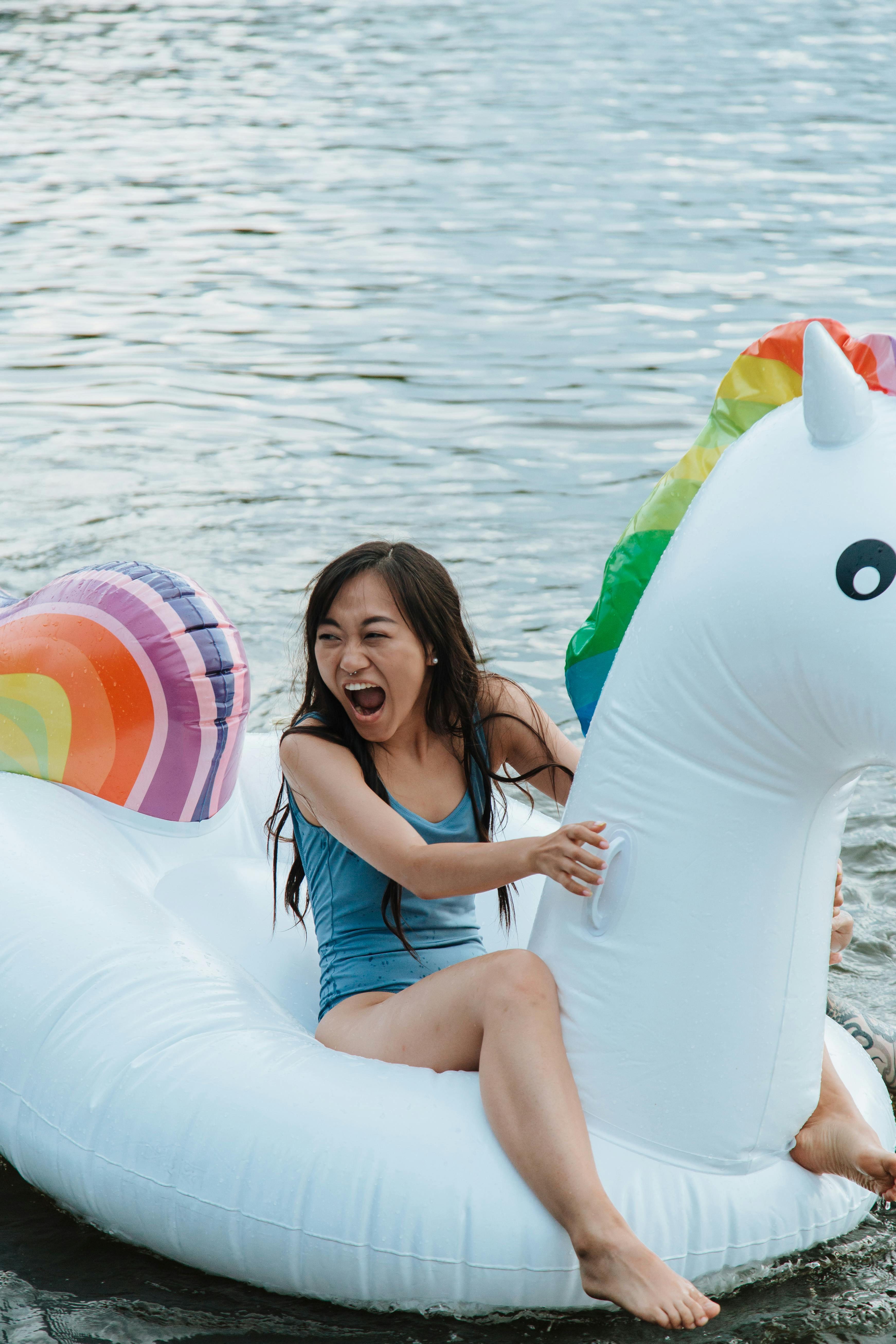 A cheerful woman enjoying a sunny day on a unicorn pool float in the water.