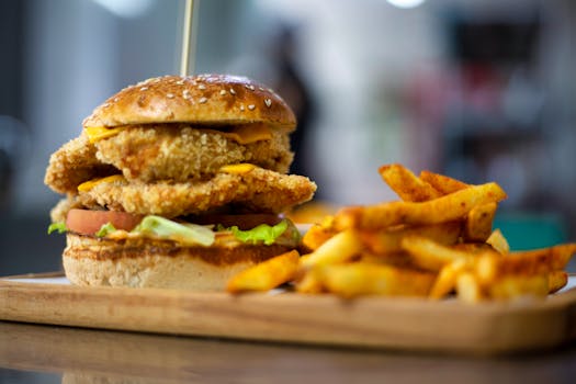 Delicious crispy chicken burger served with french fries on a wooden tray.