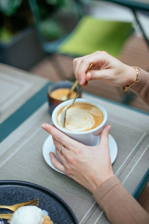 Free A woman stirs her coffee at a cafe table, showcasing a cozy and inviting lifestyle scene. Stock Photo
