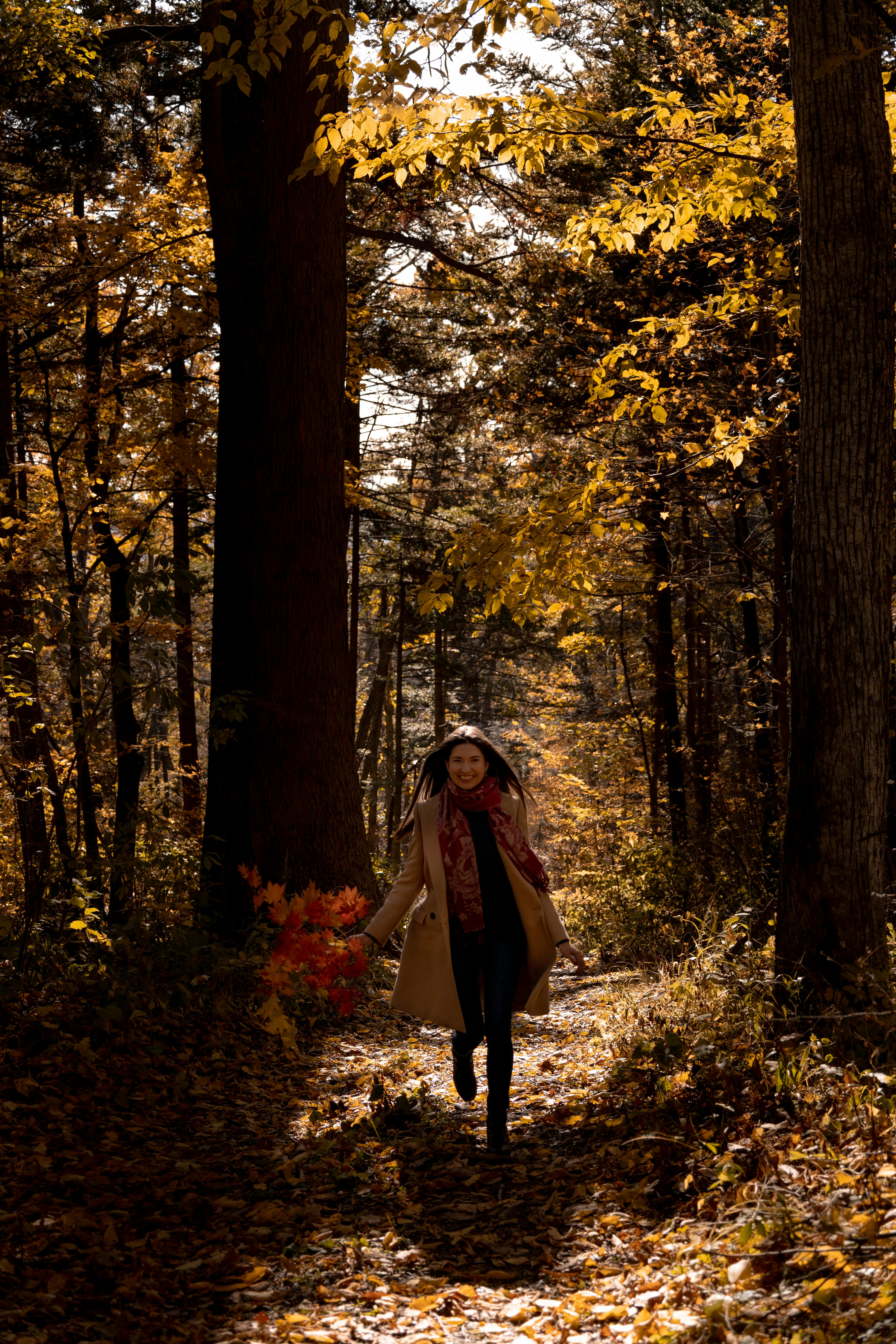 A woman joyfully runs through a vibrant autumn forest in Russia, surrounded by colorful foliage.
