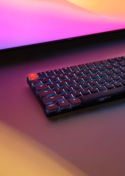 PC Keyboard Laying on Desk Before Monitor Glowing Pink