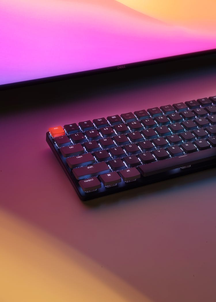 PC Keyboard Laying On Desk Before Monitor Glowing Pink