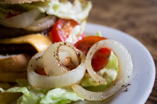 A mouthwatering close-up of a cheese burger with fresh vegetables, showcasing tomatoes, lettuce, and onions on a plate.