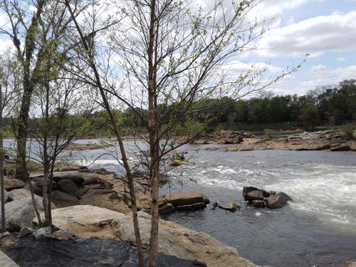 Free A scenic river view featuring rocks, trees, and rafting under a bright sky. Stock Photo