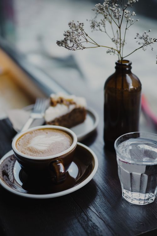 Free A warm cup of coffee with dessert and flowers on a wooden table in a cozy café. Stock Photo