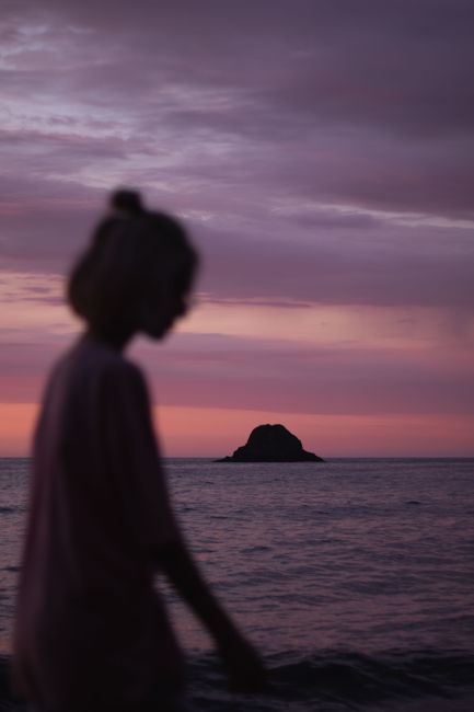 A serene silhouette of a woman by the ocean during a vivid twilight with rock and water.