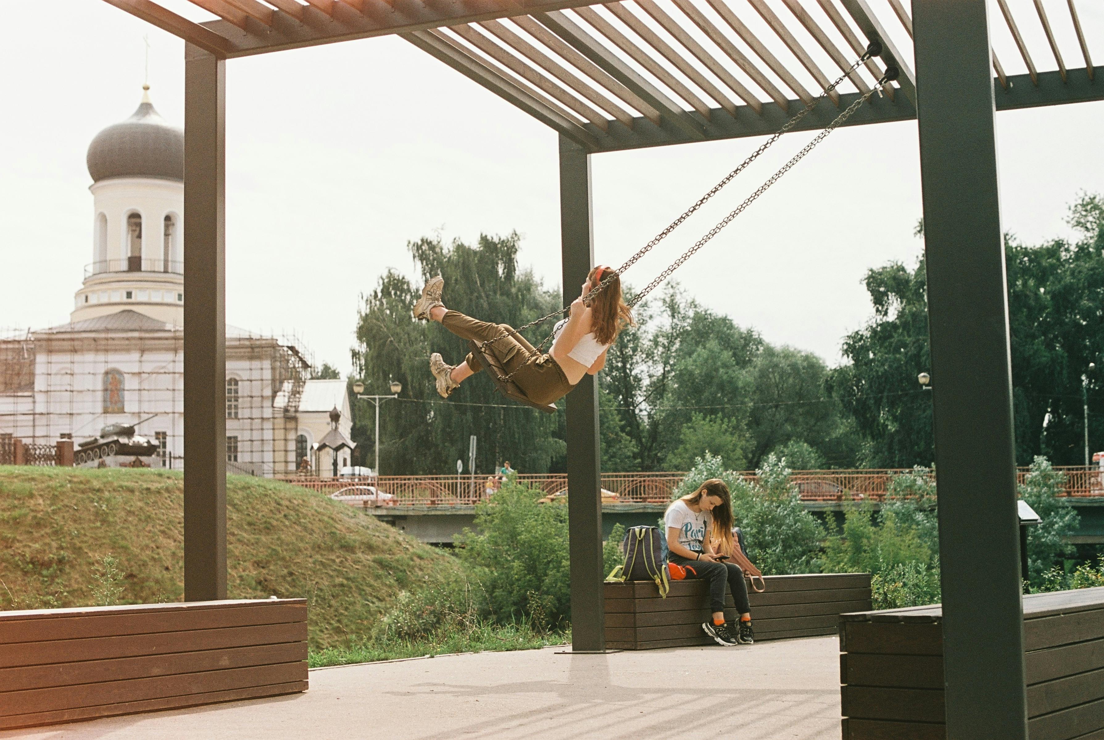 Young woman enjoying a swing in a park near a historic church in Naro-Fominsk, Russia.