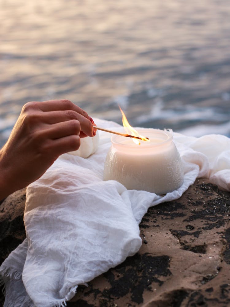 Hand Lighting Candle Sitting On White Cloth On Rock